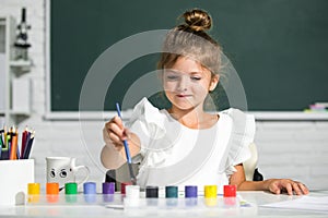 Child girl at school draws with paints. Kids artist creativity. Funny school girl face.