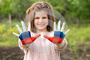 Child girl show hands painted in Russia flag colors walking outdoor, focus on hands. Day of Russian flag. Patriots