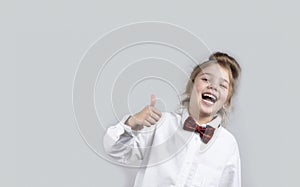 Child girl showing finger up,positive approval concept.Little caucasian female kid in white shirt with bowtie on grey background