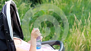 Child girl sits in a baby carriage and drinks water from a bottle.