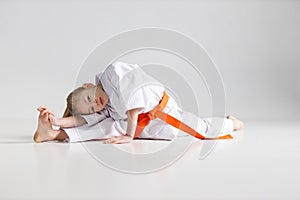 Child girl sits on a twine in a white kimono at a karate training