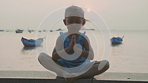 Child girl sits on the wood pier in lotus pose and meditate in slow motion