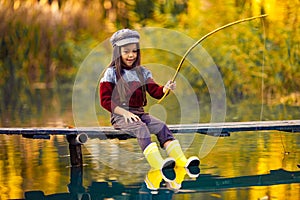 Child girl sits on wooden fishing bridge and catches fish in autumn.