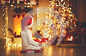 Child girl sitting back in front of Christmas tree on Christm