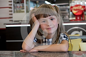 Child girl sitting in fast food restaurant behind empty table waiting for food