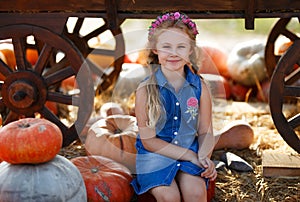 Child girl sitting between pumpkins at local farmer market in sunny autumn day
