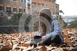 Child girl sitting on sunny autumn riverside