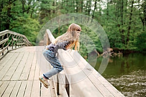 Child girl sitting on a wooden bridge near the water on the rive photo