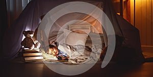 Child girl sleeping in tent with book and flashlight