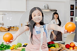 Child girl smiling hand giving or show orange fruit in home kitchen with mother