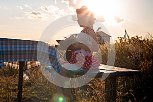 Child girl in a straw hat and dress sitting on bench and reading book. Cute kid with soft rabbit toy looking at notebook