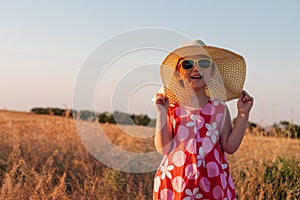 Child girl in straw hat dress in wheat field. Smiling kid in sunglasses sunset countryside. Cottagecore style aesthetic