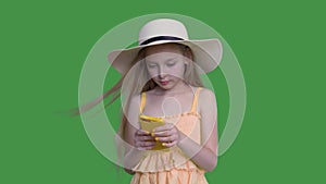 Child girl in summer hat is browsing smartphone on green wall background, alpha channel.