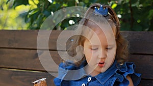 Child girl in sunglasses is eating ice cream while sitting on a bench in the park on a sunny summer day.