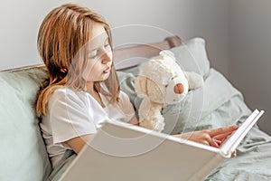 Child girl with teddy bear toy in the bed