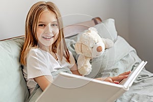 Child girl with teddy bear toy in the bed