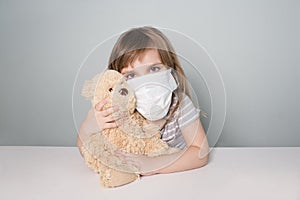 Child girl with a toy bear wearing medical face mask.