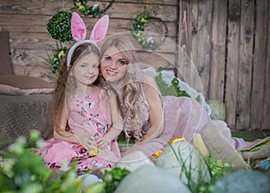 Child girl wearing bunny ears and her mother among Easter decoration in studio