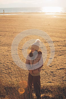 A child girl wearing the hat with a pompon standing on the beach at sunset