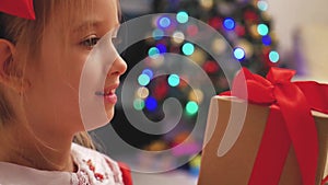 Child girl wearing a red dress opening Xmas presents. Happy little smiling girl with christmas gift box. Cozy warm