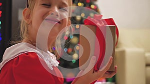 Child girl wearing a red dress opening Xmas presents. Happy little smiling girl with christmas gift box. Cozy warm