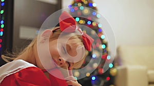 Child girl wearing a red dress opening Xmas presents. Happy little smiling girl with christmas gift box. Cozy warm