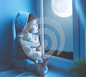 Child girl at window dreaming starry sky at bedtime