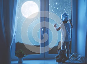 Child girl at window dreaming starry sky at bedtime