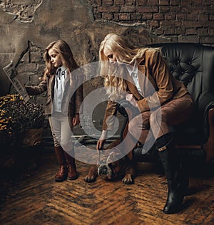 Child girl with woman in image of Sherlock Holmes read newspaper next to English bulldog on background of armchair and old interio