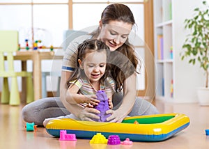 Child girl and woman mould with kinetic sand in playschool or daycare