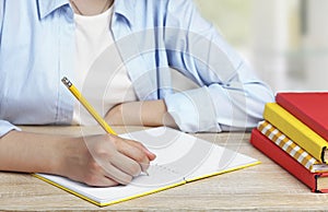 Child girl writing in copybook with pencil. Pupil at the desk, stack of books. School homework.Studing process. Education concept