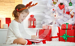 Child girl writing letter santa home near Christmas tree