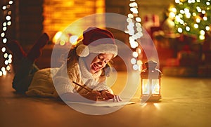 Child girl writing letter santa home near Christmas tree