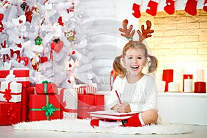 Child girl writing letter santa home near Christmas tree