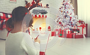 Child girl writing letter santa home near Christmas tree