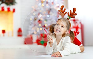 Child girl writing letter santa home near Christmas tree