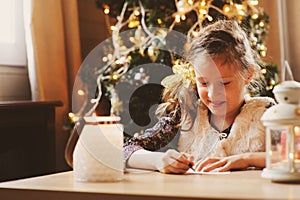 Child girl writing letter to Santa at home. 8 years old girl making gift list for Christmas or New Year at home