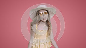 Child girl in yellow dress and hat is dancing ang singing on pink background.