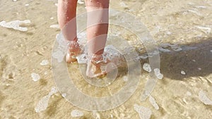 Child girls legs walking barefoot on beach coastline in ocean shallow water. Atlantic ocean beach and child walking in