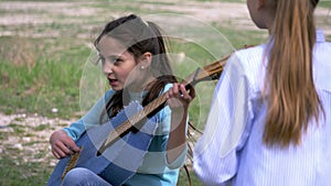 Child girls singer strum with acoustic guitar while her girlfriend standing listening music performer