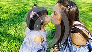 Child give flower to mom and kiss with love on green grass in park