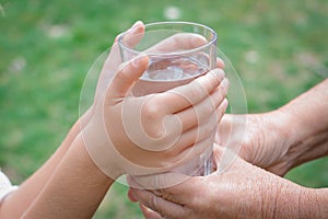 Child giving glass of water to elderly woman outdoors, closeup