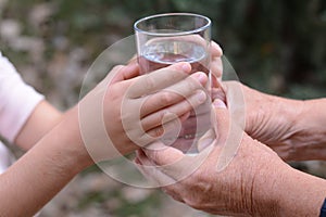 Child giving glass of water to elderly woman outdoors, closeup