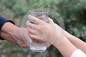 Child giving glass of water to elderly woman outdoors, closeup