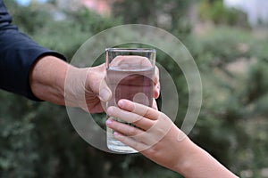 Child giving glass of water to elderly woman outdoors, closeup