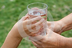 Child giving glass of water to elderly woman outdoors, closeup