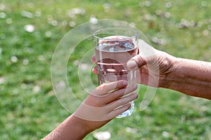 Child giving glass of water to elderly woman outdoors, closeup