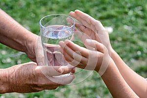 Child giving glass of water to elderly woman outdoors, closeup