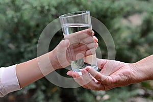 Child giving glass of water to elderly woman outdoors, closeup