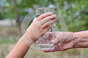 Child giving glass of water to elderly woman outdoors, closeup